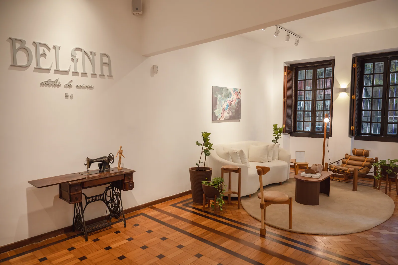 Sala da Casa Belina com o letreiro do ateliê na parede, máquina de costura antiga e piso de taco com ladrilho