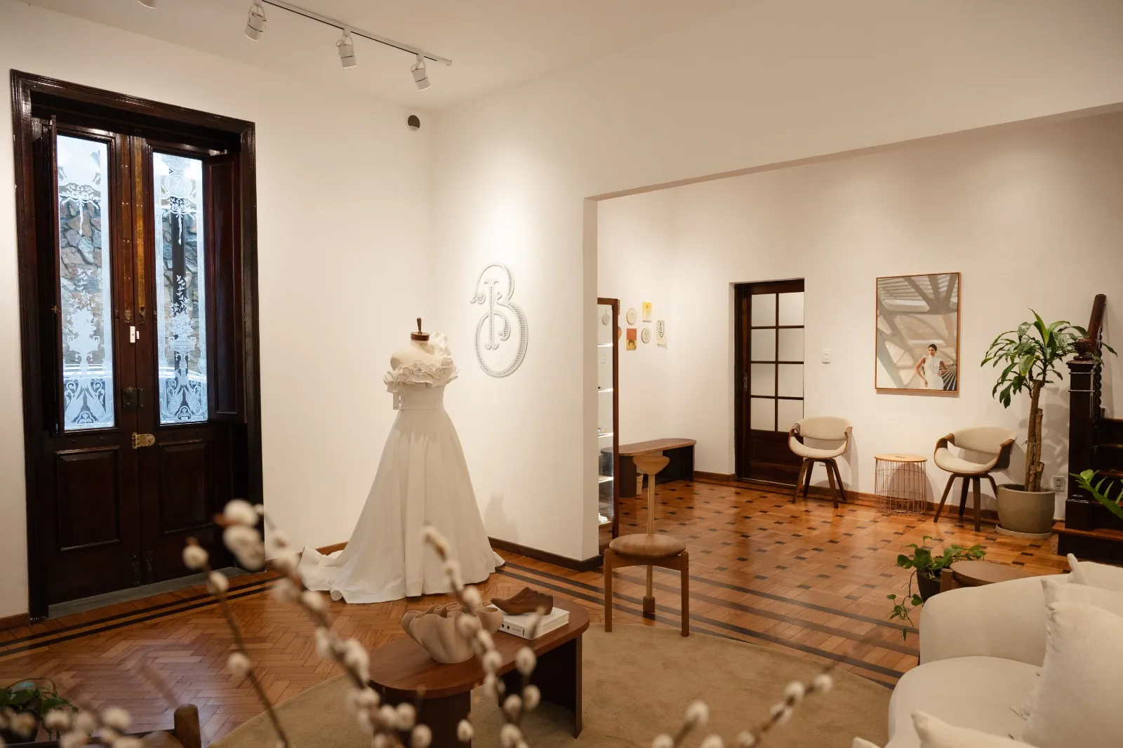 Salão da Casa Belina com vestido de noiva no manequim, o B da marca na parede e portas antigas de madeira com vidro trabalhado